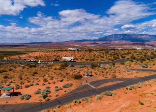 Aerial view of a desert landscape with RVs, winding roads, and distant mountains under a partly cloudy sky.