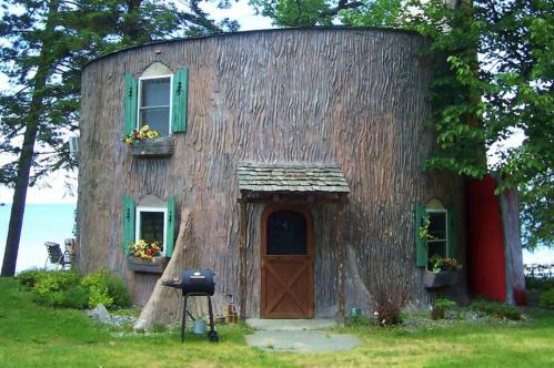 A whimsical round house designed to resemble a tree trunk, featuring green shutters and flower boxes.