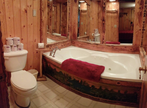 Cozy bathroom with wooden walls, a large jacuzzi tub, red towel, and a toilet, featuring multiple mirrors.
