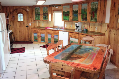Cozy kitchen with wooden cabinets, colorful artwork, a dining table, and white appliances in a rustic setting.