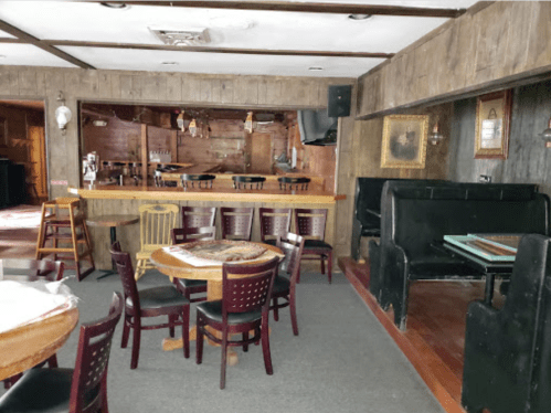 Cozy rustic interior of a bar with wooden walls, tables, and chairs, featuring a counter and a few decorative elements.