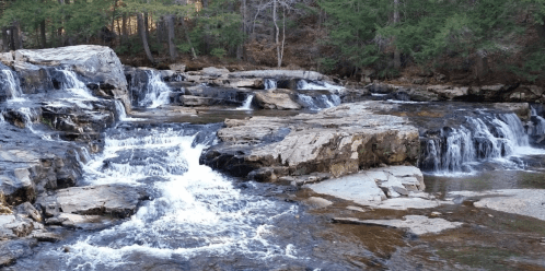 A serene waterfall cascading over rocky terrain, surrounded by lush green trees.