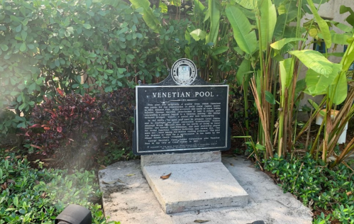 A historical plaque titled "Venetian Pool" surrounded by lush greenery and tropical plants.
