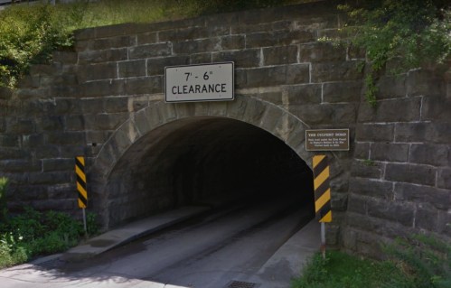 A stone archway tunnel with a clearance sign reading "7'-6''" and caution stripes on the sides.