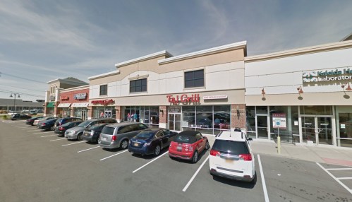 A shopping plaza with several storefronts, including Tai Grill, and a parking lot filled with cars.