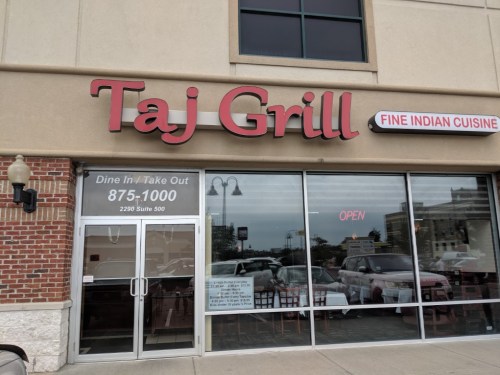 Exterior of Taj Grill restaurant, featuring a large sign and glass entrance, with "OPEN" displayed.