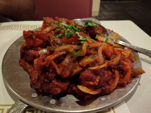 A silver platter filled with spicy red meat, onions, and green peppers, garnished with fresh cilantro.
