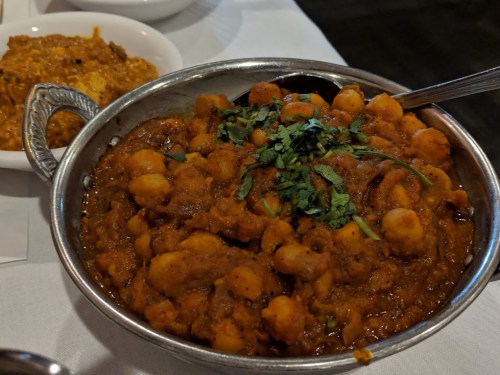 A bowl of chickpea curry garnished with fresh cilantro, served with a side dish in the background.