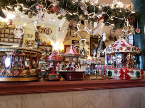 Colorful carousel figurines displayed on a shelf, adorned with festive decorations and twinkling lights.