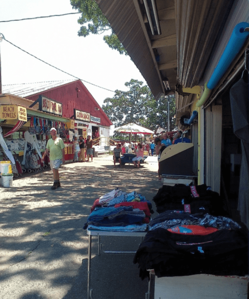 A sunny outdoor market scene with colorful stalls, people browsing, and clothing displayed on tables.