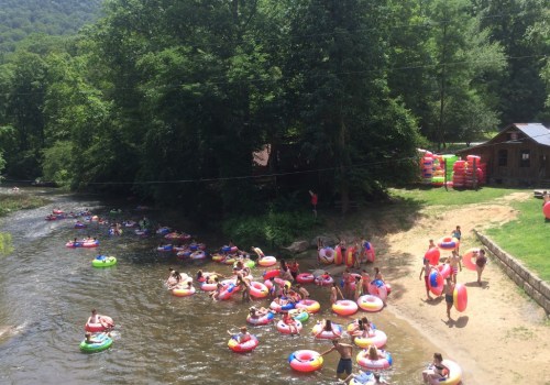 A lively river scene with people floating on colorful tubes, surrounded by trees and a sandy bank.