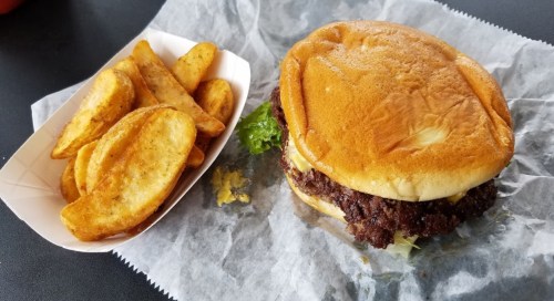 A juicy burger with lettuce on a bun, served with a side of golden potato wedges on parchment paper.