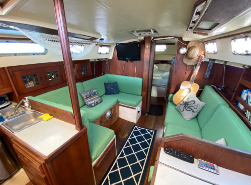 Interior of a sailboat featuring green seating, a small kitchen area, and a cozy living space with nautical decor.