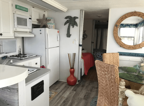 Cozy beach-themed interior with a kitchen, dining area, and a glimpse of a bedroom in a mobile home.