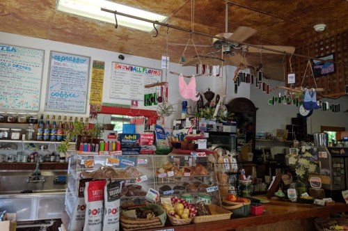 A cozy café interior with a counter displaying baked goods, drinks, and colorful decorations hanging from the ceiling.