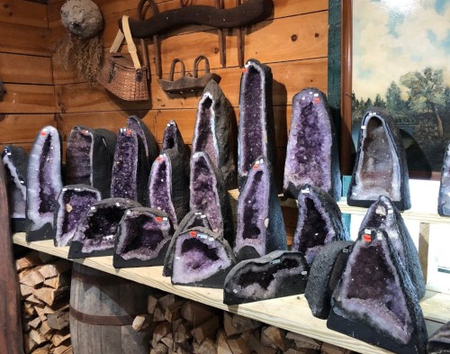 A display of various amethyst geodes on a wooden shelf in a rustic setting.