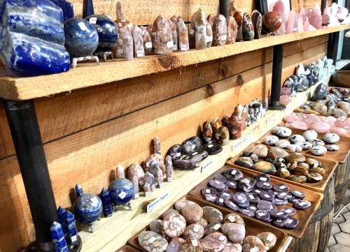 A display of various gemstones and crystals arranged on wooden shelves, showcasing different shapes and colors.