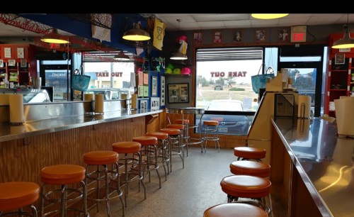 A colorful diner interior with orange stools, a long counter, and large windows showing a view outside.