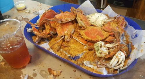 A blue tray filled with seasoned crabs and a cup of iced tea on a table.