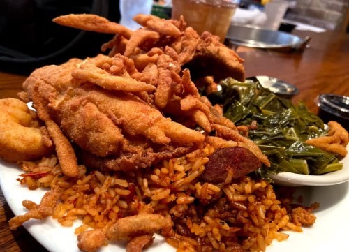 A plate of fried catfish, seasoned rice, collard greens, and crispy onion rings.