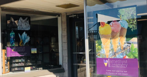 A storefront with a sign for Amethyst Creamery, featuring colorful ice cream cones and displays of crystals inside.