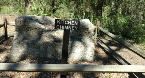 A large stone structure labeled "Kitchen Chimney" surrounded by a wooden fence in a wooded area.