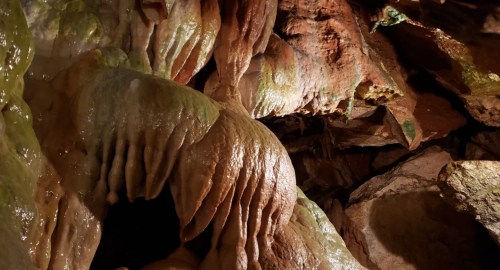 Close-up of textured cave formations with colorful mineral deposits and intricate shapes in a dimly lit environment.