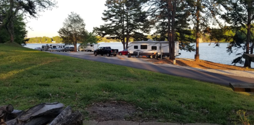 A scenic view of a lakeside campground with RVs parked along a tree-lined road.
