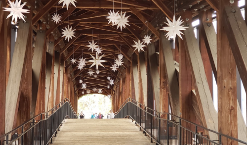 A wooden bridge with star-shaped decorations hanging from the ceiling, leading to a bright exit in the distance.