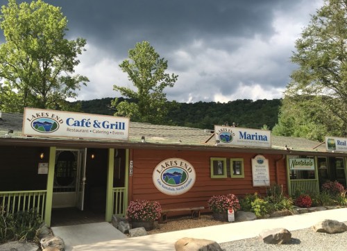 Exterior view of Lakes End Café & Grill, Marina, and Real Estate office, surrounded by trees and a cloudy sky.