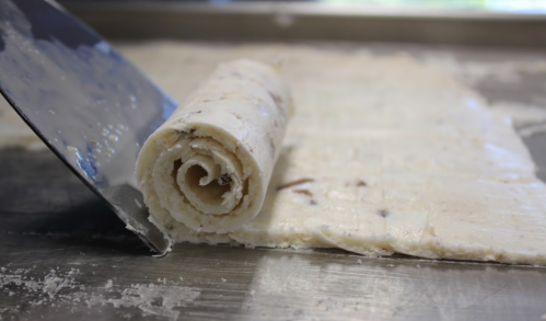 Close-up of a rolled ice cream dessert on a metal surface, with a spatula nearby.