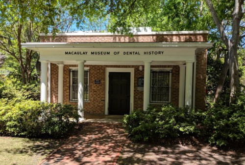 Exterior of the Macaulay Museum of Dental History, featuring brick architecture and surrounded by greenery.