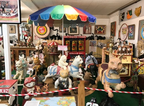 A colorful vintage carnival scene filled with whimsical animal figures and games under a striped umbrella.