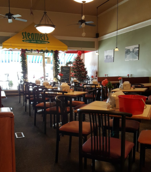 Cozy restaurant interior with tables, chairs, a Christmas tree, and festive decorations under a yellow awning.