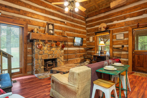 Cozy log cabin interior with a stone fireplace, wooden beams, and rustic furniture, creating a warm atmosphere.