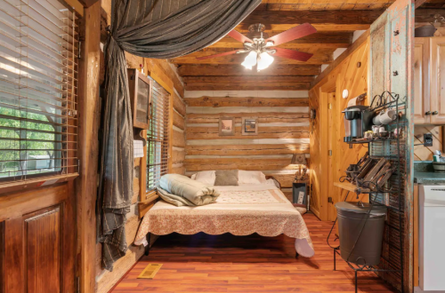 Cozy log cabin bedroom with a bed, wooden walls, ceiling fan, and rustic decor. Warm and inviting atmosphere.