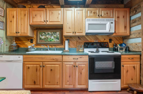Cozy kitchen with wooden cabinets, a microwave, stove, and a rustic decor featuring a framed painting.