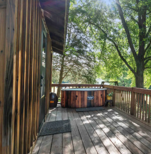 A wooden deck with a hot tub surrounded by trees and sunlight filtering through the leaves.