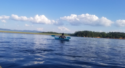A person kayaking on a calm lake with blue skies and fluffy clouds in the background.