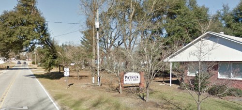 Sign for Patrick Town Hall beside a road, with trees and a residential building in the background.