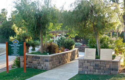 Entrance to a sensory garden with a sign and landscaped pathways surrounded by greenery and flowers.