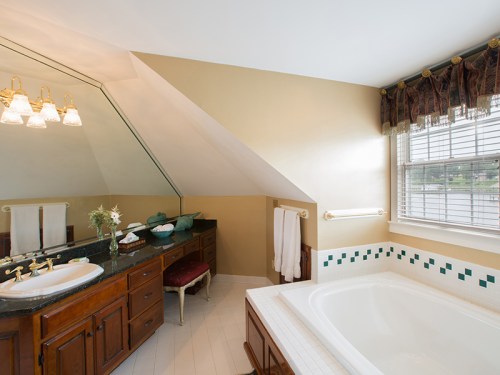 Bright bathroom featuring a large tub, dark wood vanity, and a sloped ceiling with elegant lighting and decor.