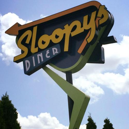 Sign for Sloopy's Diner with a retro design, featuring bright colors and a blue sky in the background.