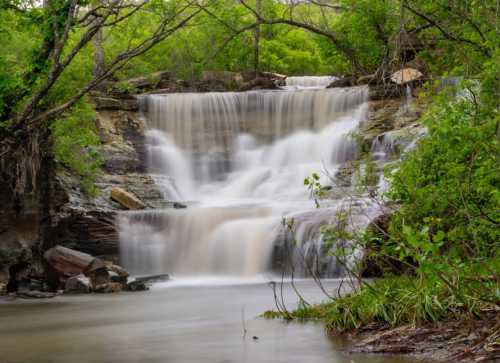 A serene waterfall cascades over rocks, surrounded by lush green foliage and trees.