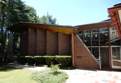 A modern brick building with large windows, surrounded by greenery and a clear blue sky.