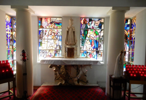 A serene chapel with stained glass windows, a marble altar, and lit candles, creating a peaceful atmosphere.