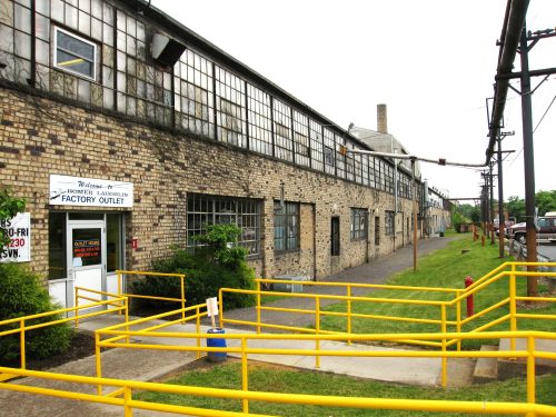 A brick building with large windows and a yellow railing leading to a factory outlet entrance.