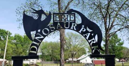 Archway sign for Erie Dinosaur Park, featuring dinosaur silhouettes and greenery in the background.