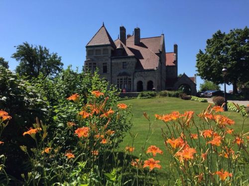A historic mansion surrounded by vibrant orange flowers and lush greenery under a clear blue sky.