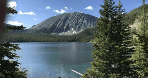 A serene lake surrounded by trees, with a mountain in the background under a clear blue sky.